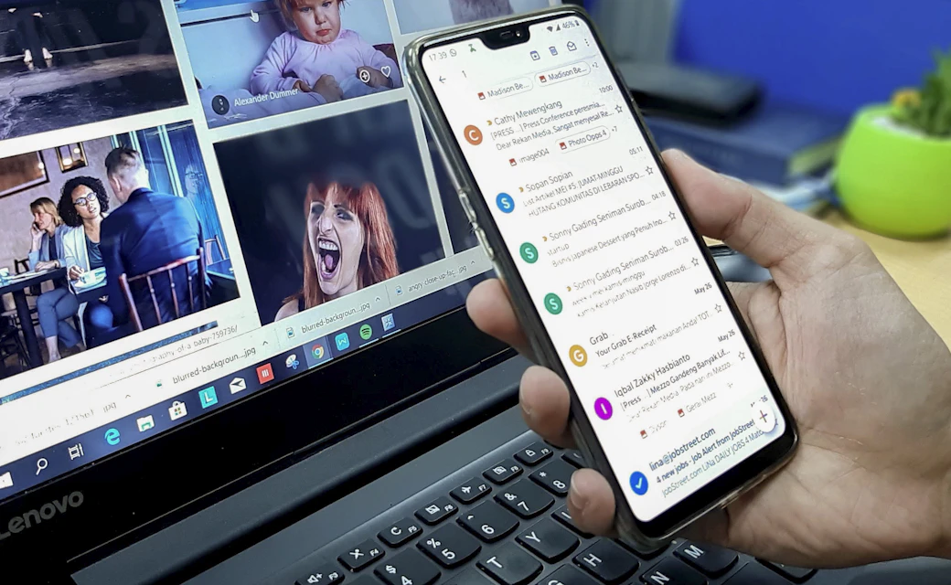 Persona gestionando mensajes desde un celular y un portátil.